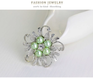 Macro detail of silver flower brooch with light green pearls and crystal accent