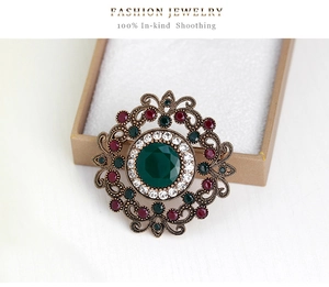Macro shot of vintage baroque brooch with green crystal and red stones on a beige gift box