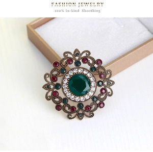 Macro shot of luxury vintage round brooch with emerald-cut green stone and intricate filigree