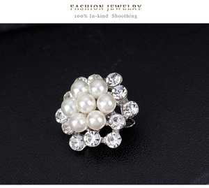 Dettaglio macro della spilla a fiore argento con perle finte bianche e strass brillanti