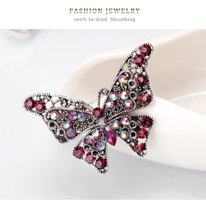 Dettaglio macro della spilla a farfalla vintage con strass rossi e filigrana argento