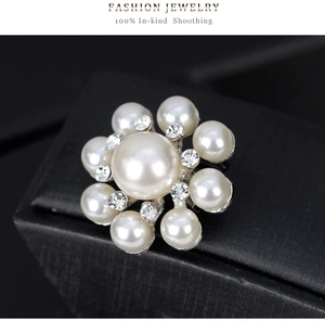 Détail macro d'une broche en forme de fleur avec une perle centrale et des strass brillants