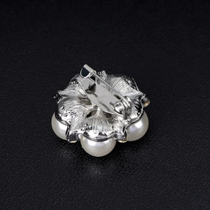 Elegant silver floral brooch with pearls and safety pin closure on black background