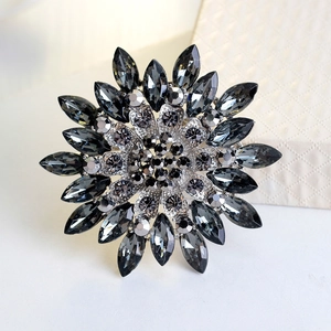 Sunflower brooch with silver base and dark grey rhinestones on white surface
