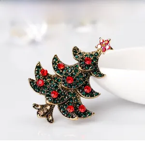 Détail d'une broche sapin de Noël avec strass verts et rouges sur une base dorée