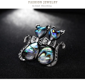 Detailed close-up of double cat brooch with iridescent abalone shell and black stones