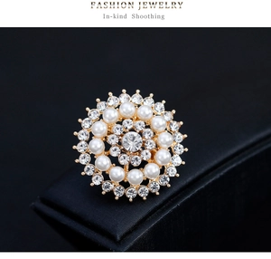 Détail d'une broche tournesol avec perles blanches et strass brillants sur base dorée