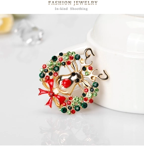 Détail d'une broche couronne de Noël avec élan doré, nœud rouge et strass colorés
