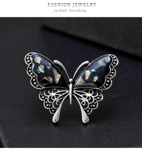 Macro shot of silver butterfly brooch with iridescent shell wings on dark leather background