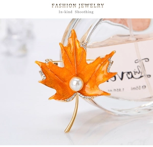 Détail de la broche feuille d'érable en émail orange avec strass et perle blanche