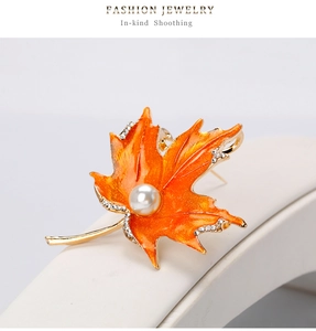 Détail macro de broche feuille d'érable en émail orange, strass et perle blanche