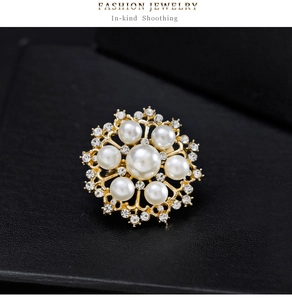 Gros plan sur la broche fleur dorée avec une grande perle blanche et des strass brillants