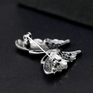 Silver butterfly brooch with detailed wing textures and secure pin clasp on black leather