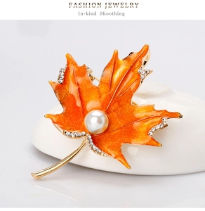 Détails macro d'une broche en forme de feuille d'érable orange avec des perles