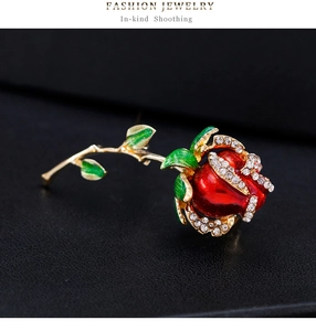 Macro d'une broche rose en émail rouge avec feuilles vertes et cristaux sur fond noir