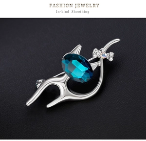 Détail d'une broche chat argentée avec un cristal bleu foncé sur fond de cuir noir texturé