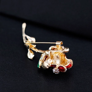 Élégante broche rose dorée avec émail rouge et cristaux sur fond de cuir noir texturé