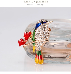 Detail of colorful bird brooch with sparkling rhinestones perched on golden flower branch
