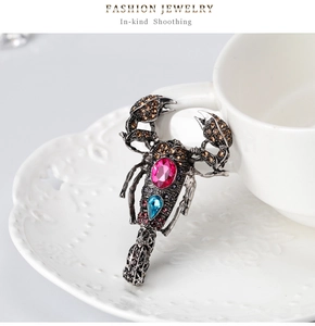 Detailed close-up of retro scorpion brooch with pink and blue stones on white ceramic