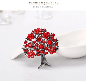Dettaglio spilla ad albero color argento con cristalli rossi su ceramica bianca
