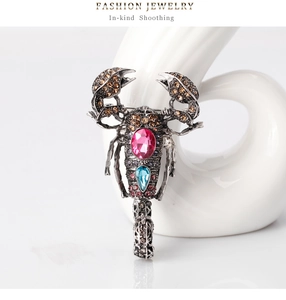 Detailed close-up of a vintage scorpion brooch featuring pink crystals and blue gemstones