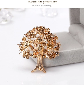 Macro di una spilla ad albero dorata con strass ambra su superficie bianca lucida