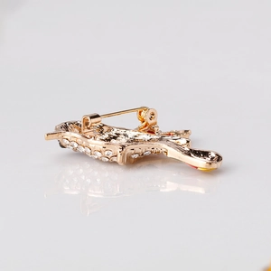 Golden bird brooch with colorful oil drip and crystals on a minimalist reflective surface