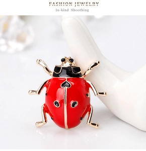 Close-up of a red and gold ladybug brooch with heart detail on a ceramic hand display