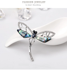 Detailed view of dragonfly brooch with blue crystals and iridescent shell inlays