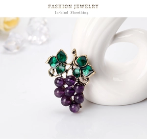 Dettaglio di un'elegante spilla a uva con foglie in smalto verde e perle viola su base oro