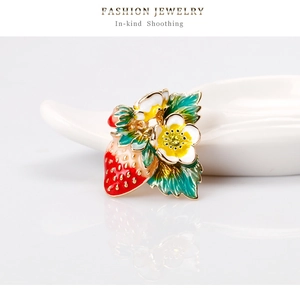 Macro d'une broche fraise et fleur en émail coloré sur un socle blanc réfléchissant