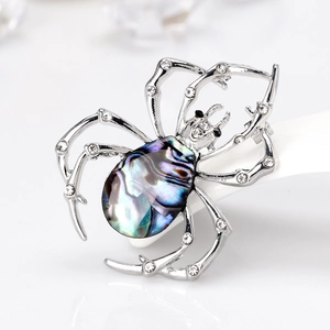Broche araignée avec incrustation de nacre irisante et strass brillants sur fond blanc