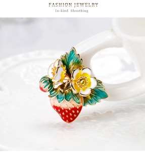 Détail macro de broche fraise en émail rouge avec fleurs blanches et graines d'or