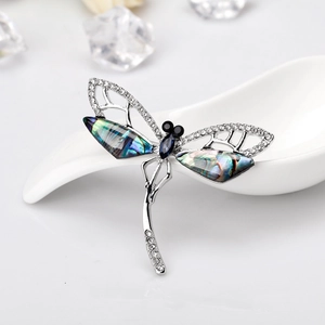 Vintage dragonfly brooch with colorful abalone wings and sparkling crystals on a ceramic spoon