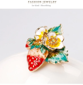 Vue macro de la broche fraise avec émail rouge et détails floraux plaqués or élégants
