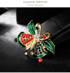 Macro shot of gold Christmas bell brooch with red and green crystals and holly leaves