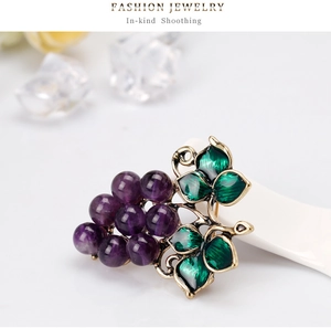 Dettaglio di una spilla a uva viola vintage con foglie in smalto verde su supporto