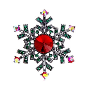 Macro shot of snowflake brooch with faceted red center stone and green crystal accents