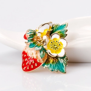 Broche fraise élégante en émail rouge avec cristaux sur une surface blanche réfléchissante