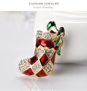 Détail macro d'une broche botte de Noël avec émail rouge, nœud vert et strass brillants