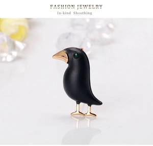 Detailed close-up of a black crow brooch with green gem eye and golden metal beak and claws