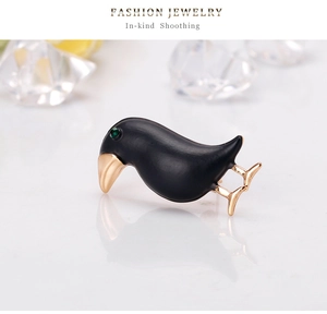Macro detail of black enamel bird brooch with golden beak and green gemstone eye