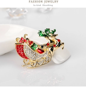 Detailed view of a golden reindeer sleigh brooch with colorful rhinestones on a white surface