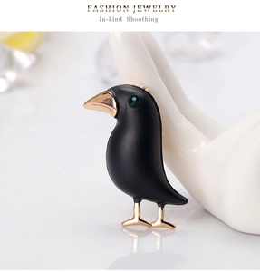 Detail of artistic black crow brooch with green gemstone eye on ceramic hand display