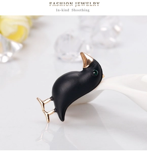 Detailed close-up of a matte black bird brooch with gold beak and green gemstone eye