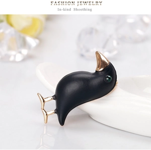 Detail of matte black bird brooch with gold beak and green crystal eye on ceramic base