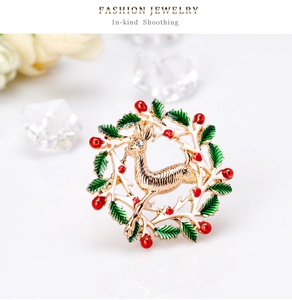 Détail d'une broche couronne renne de Noël avec feuilles d'émail vert et baies rouges