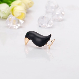 Creative black crow bird brooch with gold beak and green eye accent on white background
