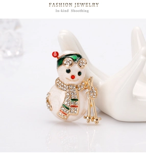 Macro detail of skiing snowman brooch with white enamel, rhinestones and gold accents