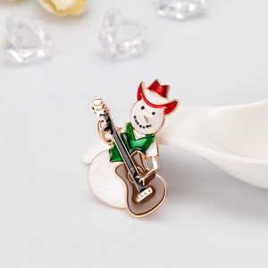 Detail einer Schneemann-Emaille-Brosche mit rotem Hut und Gitarre auf weißer Oberfläche